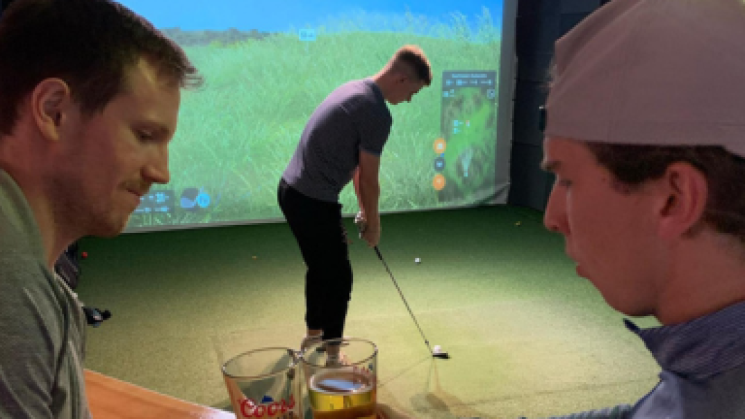 2 guys drinking beer while another plays virtual golf